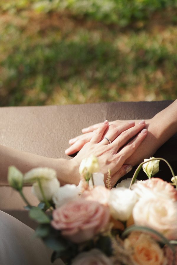 Close-up of hands and wedding ring resting on a bouquet